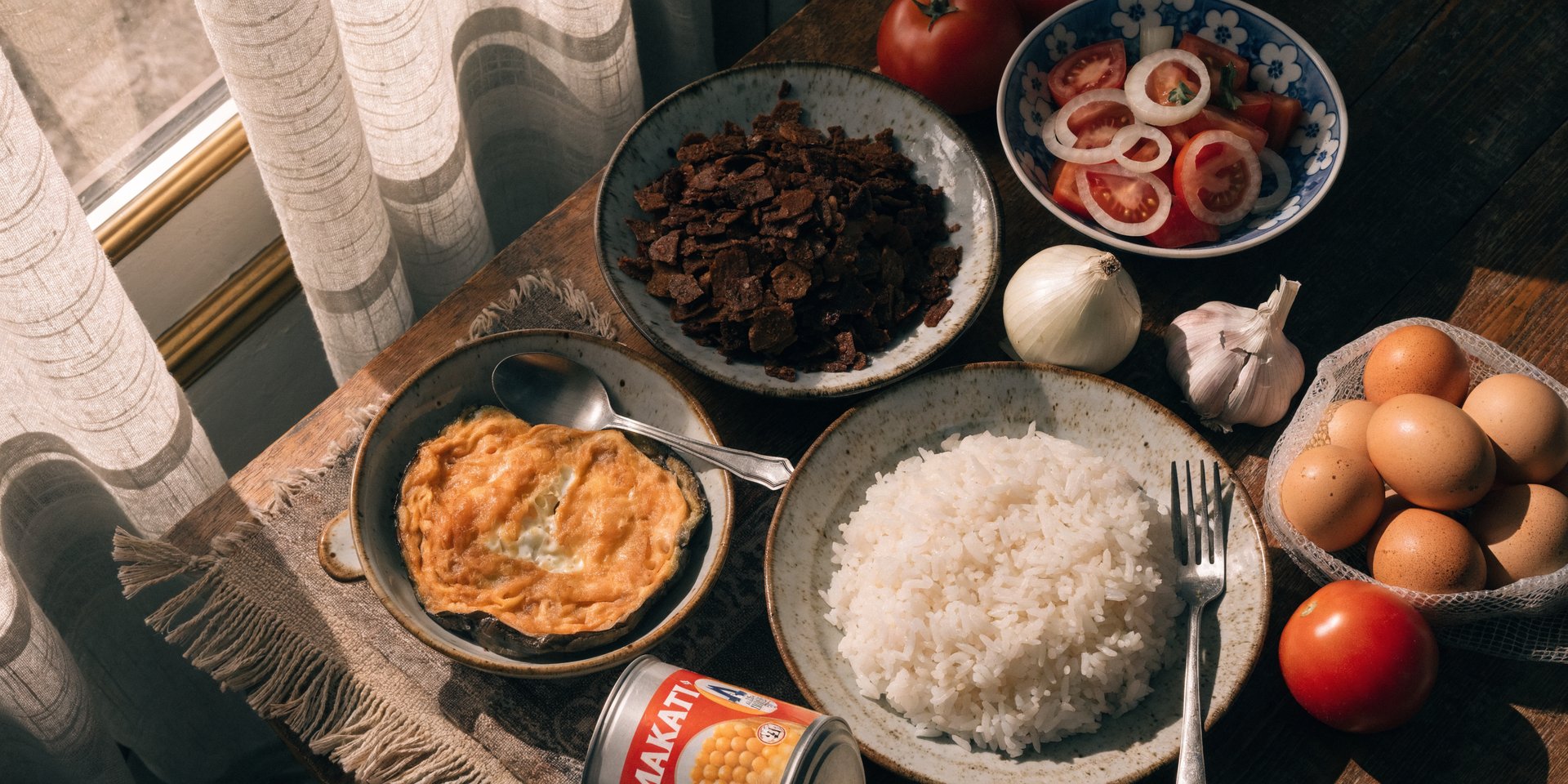 Tortang talong, white rice, sardines, eggs, and tomatoes arranged on a wooden table