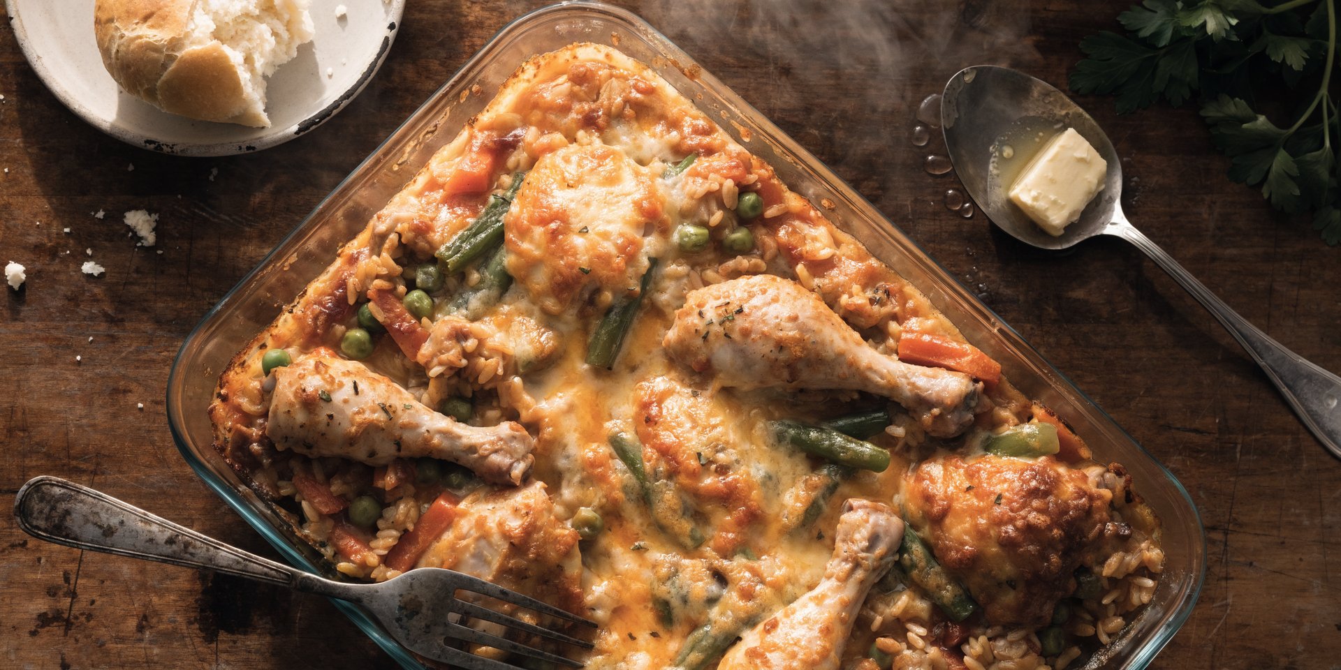 A golden-brown chicken and rice casserole in a glass baking dish sits on a wooden table, fresh from the oven.