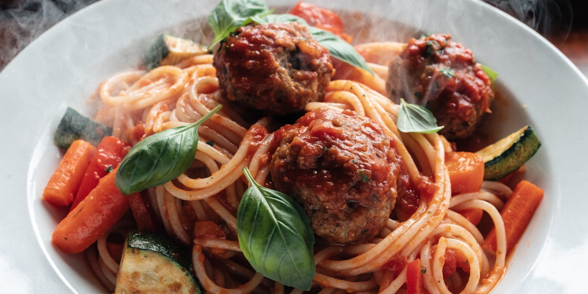 A close-up overhead photograph of a bowl of spaghetti and meatballs with fresh basil on top.